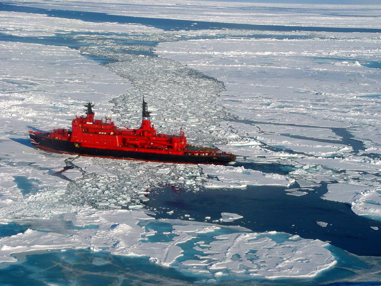 A red icebreaker ship sailing through sheet ice.
