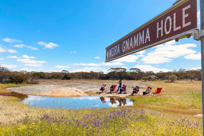 A group of people are sitting on red deck chairs around a natural water hole