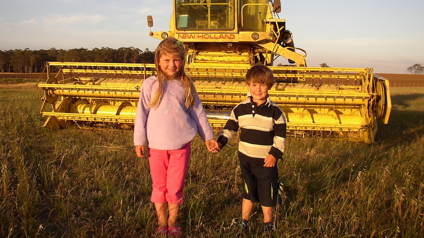 a boy and girl hold hands in front of a large grain harvester