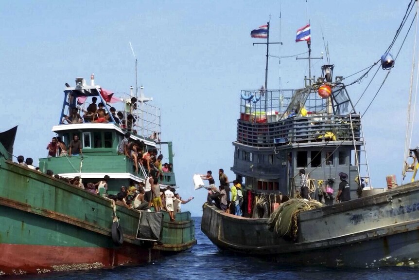 Thai fishermen (R) give some supplies to migrants on a boat.