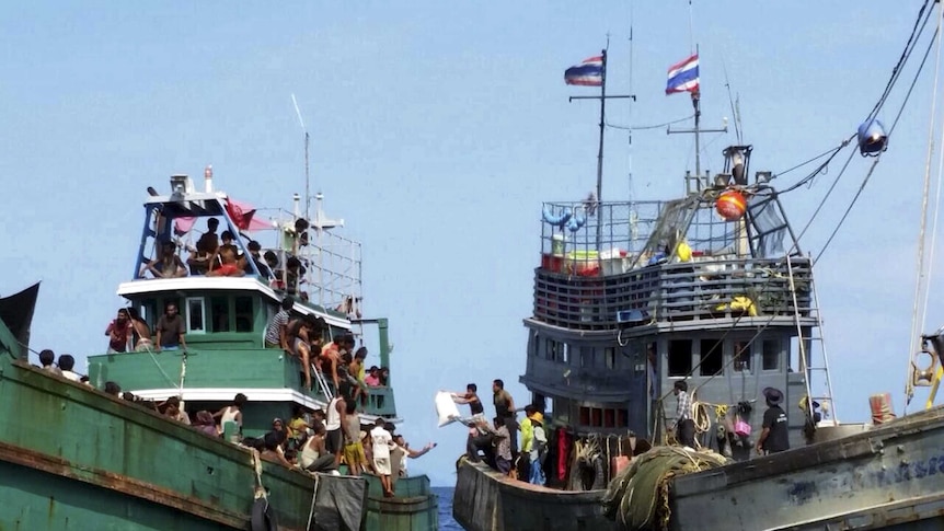 Thai fishermen give supplies to migrants on a boat