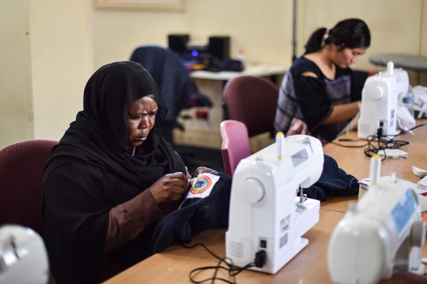 Amira (left) from Sudan is sitting in front of a sewing machine andis   one of the refugees working on the project.