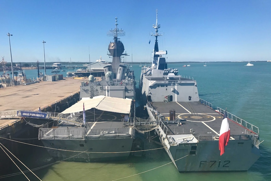 Two smaller warships sit aside one another docked in Darwin port on a sunny day.