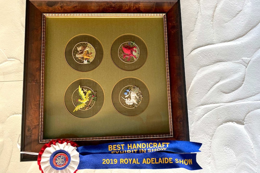 A golden embroidery framed with wood and with a winner's sash beneath.