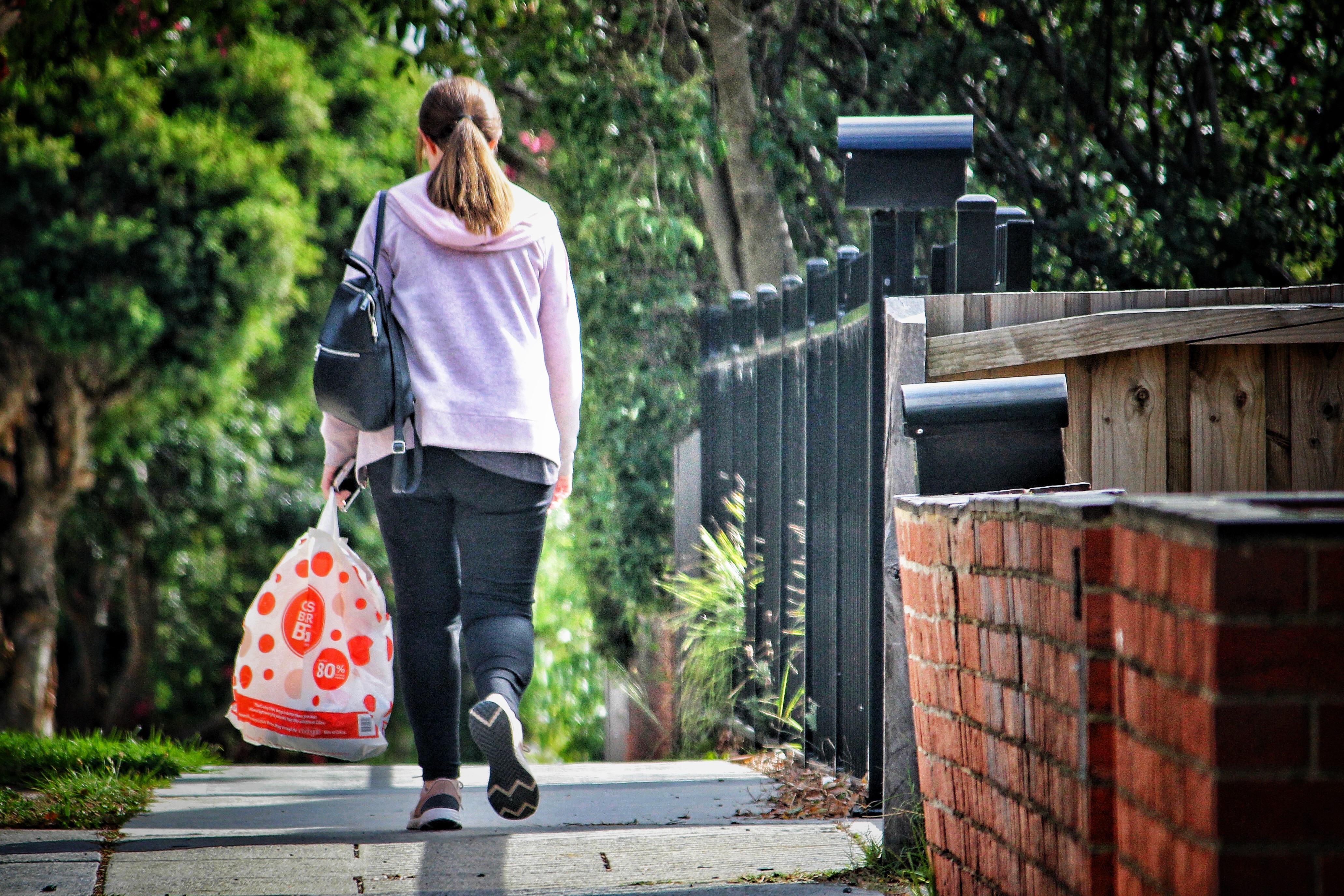 Woman wearing pink cardigan walking down a street holding a shopping bag 