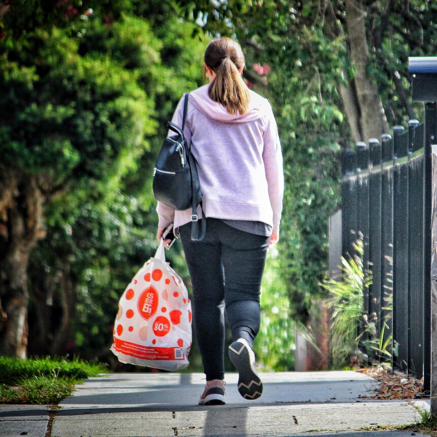 Woman wearing pink cardigan walking down a street holding a shopping bag 