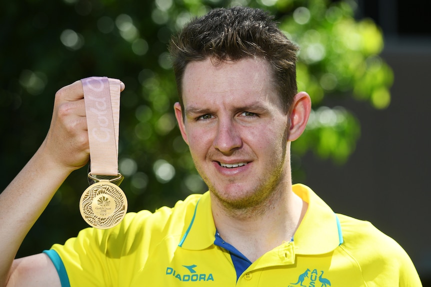 A man wearing a yellow shirt holds up a gold medal
