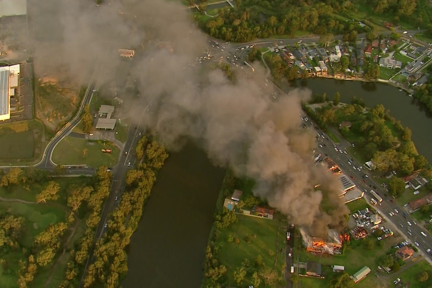 Black smoke billowing out from a burning building next to a river