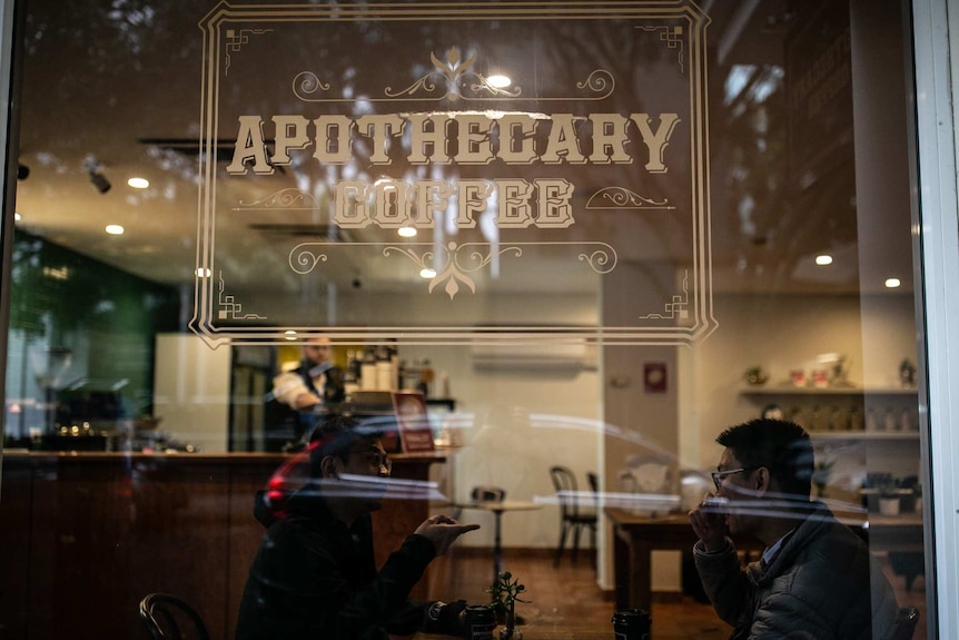 the outside of a coffee shop with people at a table behind the window