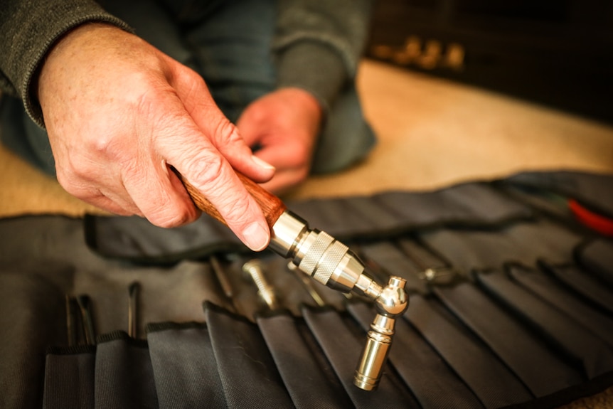 A close of up of Graeme's hands holding a tuning hammer with his tool bag underneath.