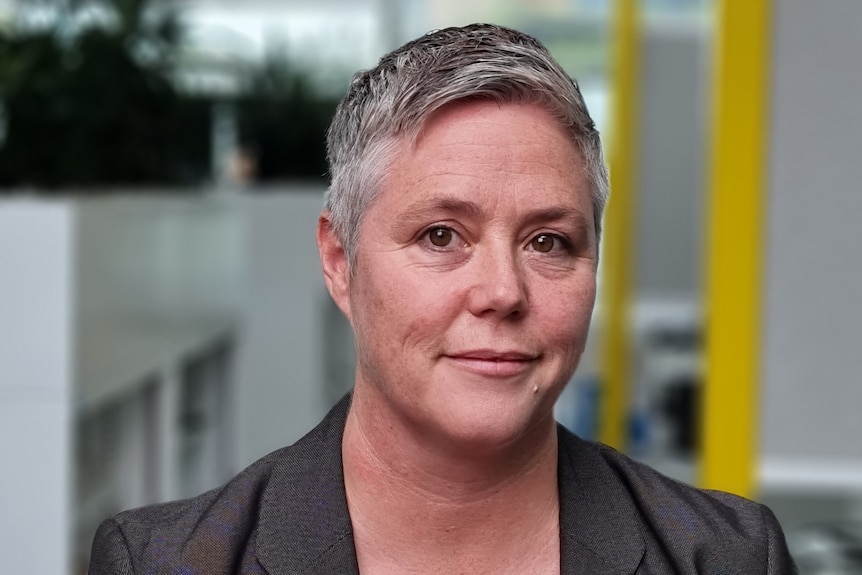 A woman with short hair wearing a grey jacket.