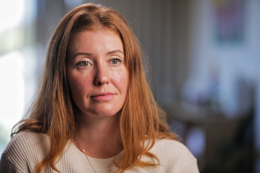 Woman with red hair, wearing a white t-shirt, looks ahead.