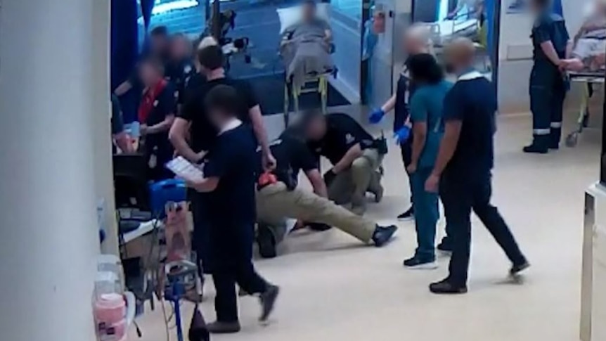 A chaotic scene with several people on the ground in a hospital, all of them with blurred faces. 