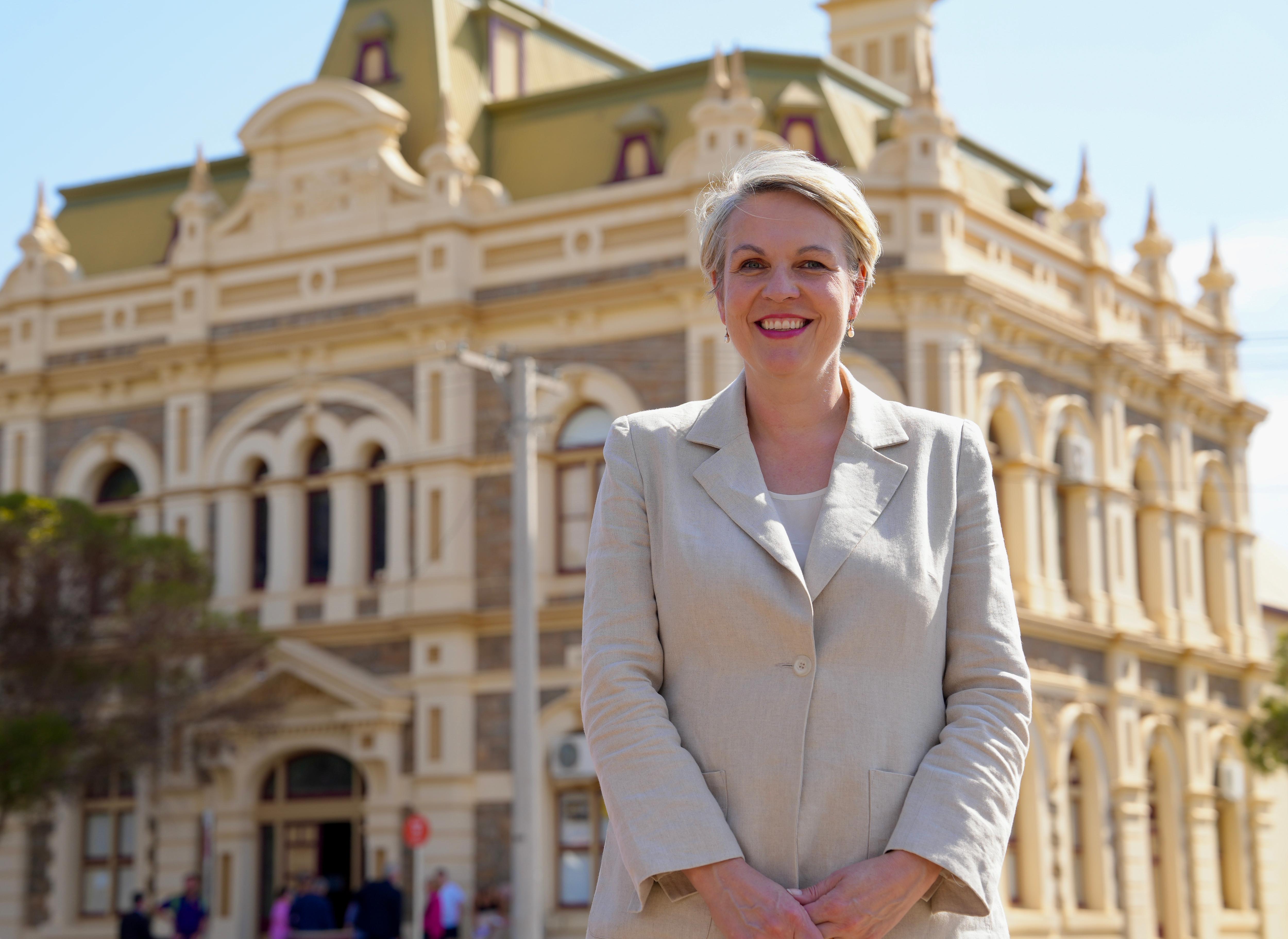 A white woman wearing beige cloths smiles while standing in front of the Broken Hill trades hall