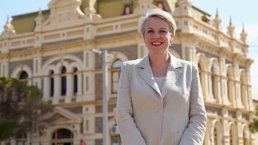 A white woman wearing beige cloths smiles while standing in front of the Broken Hill trades hall