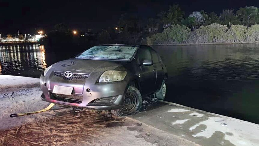 A waterlogged silver car on the edge of a lake at night.