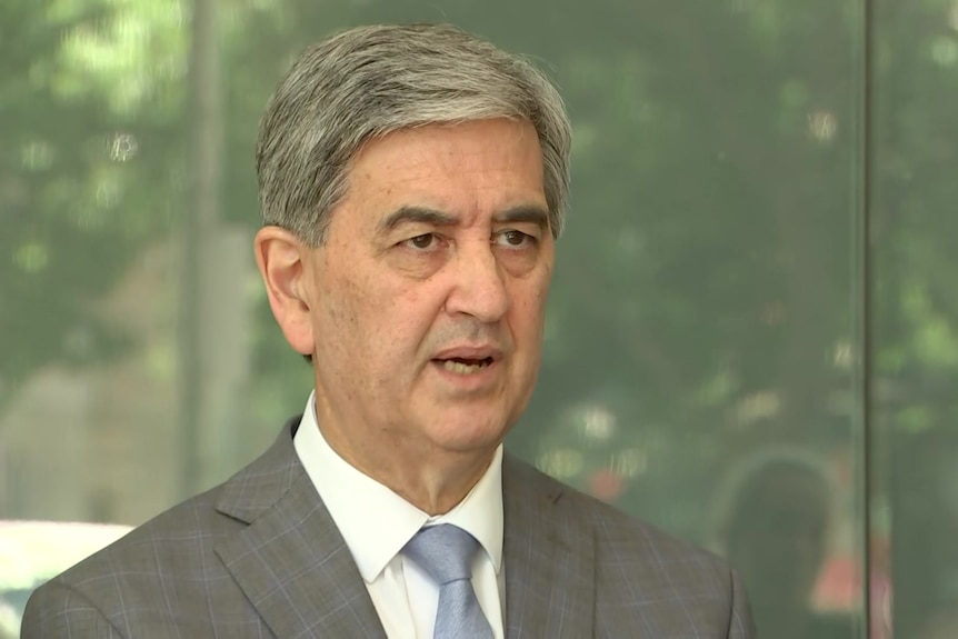 A gray haired man wearing a gray suit and a blue tie