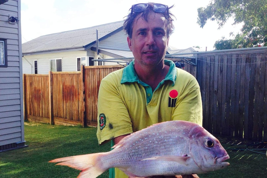 David Murphy, wearing sunglasses on his head, stands in a backyard holding a fish.