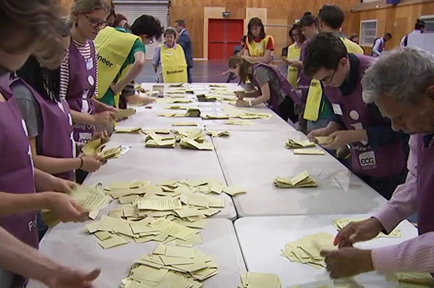 Electoral Commission Queensland volunteers counting votes on a long table