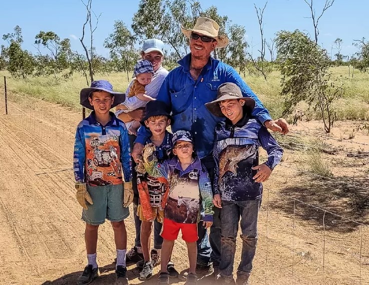 A family stand in front of a fence on their property