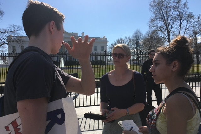 March holding microphone interviewing student outside White House.
