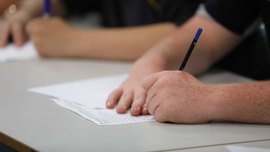 A boy writes with a pencil in a classroom.