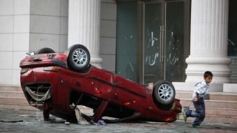 Photo shows a damaged, overturned red car with a child running alongside.