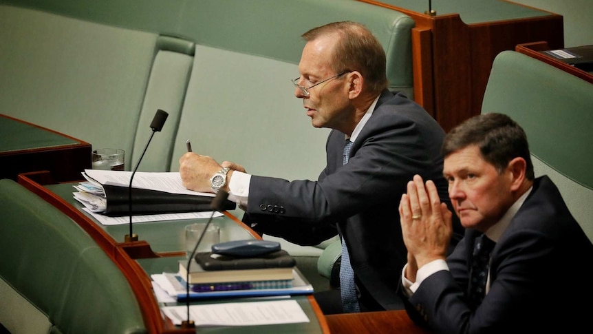 Former PM Tony Abbott does some paperwork during Question Time. He's wearing glasses and sitting next to Kevin Andrews