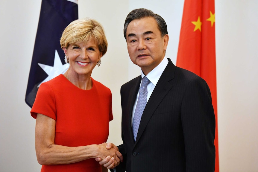 Julie Bishop and Wang Yi shake hands while standing in front of Australian and Chinese flags.