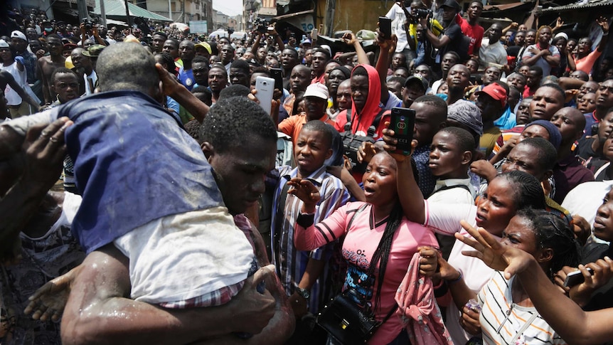 Looking down an orange spinal board, a crowd of rescuers place a child in a dusty blue shirt onto the board.