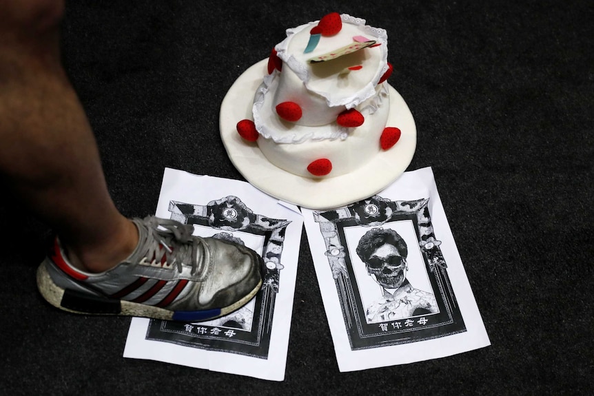 A sports shoe with a man's leg steps on photocopies of woman on ground next to a white cake.