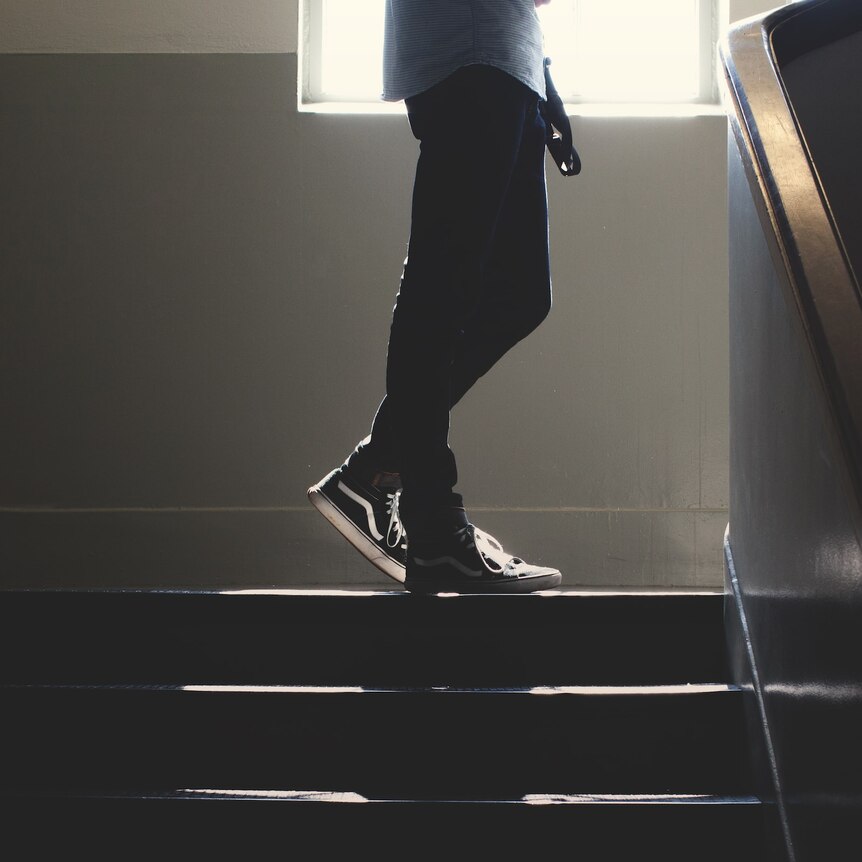legs of a young person in jeans in a dark stairwell. 