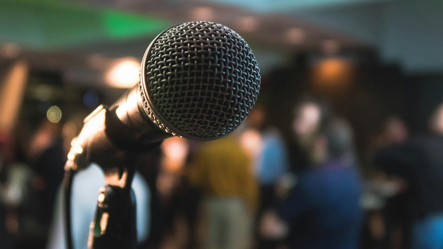 A microphone on a stand in front of a crowd. 