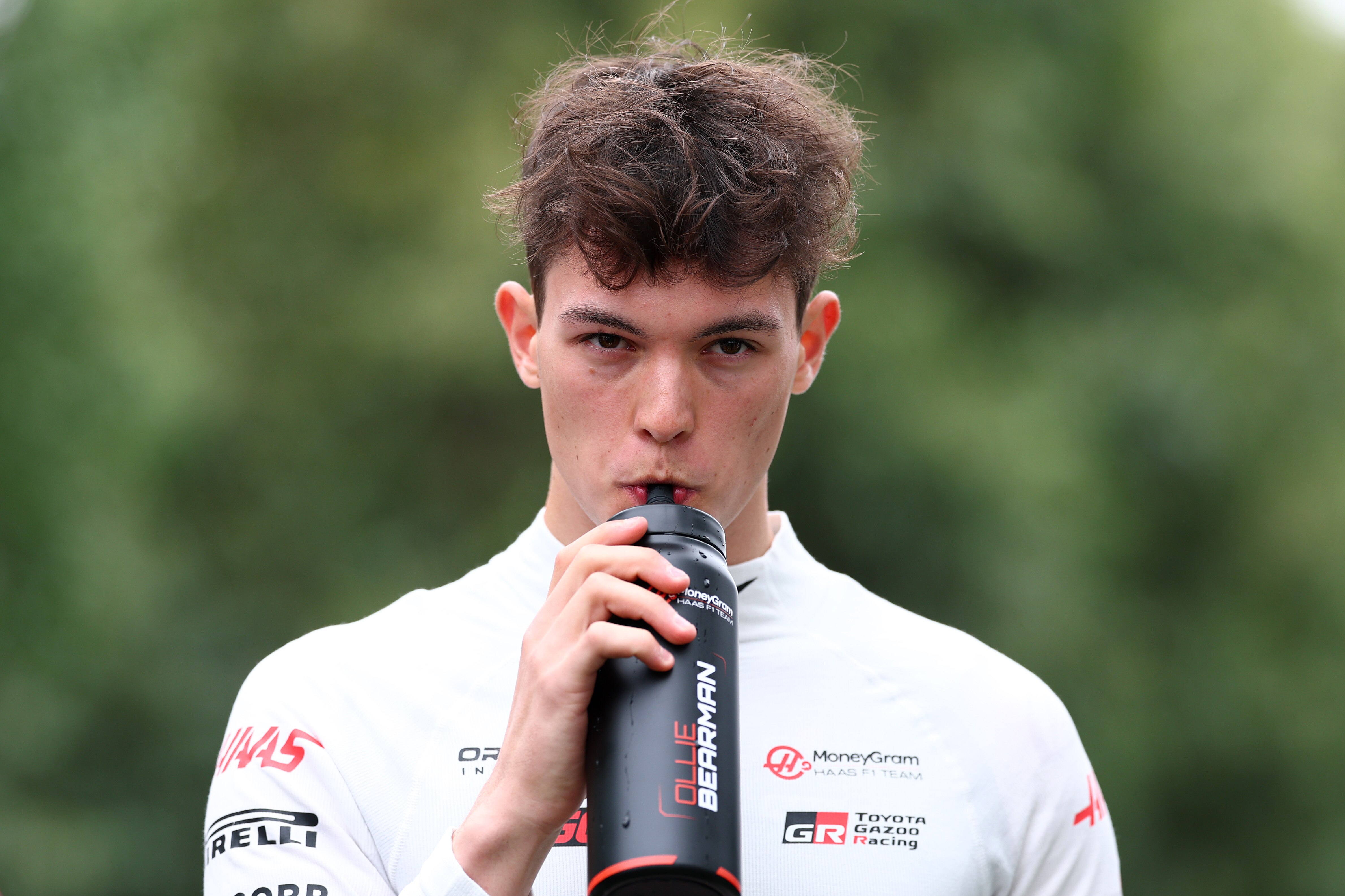 Oliver Bearman walking through the F1 paddock, drinking from a bottle