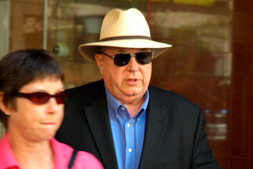 A man with sunglasses and a hat walks out of a government office
