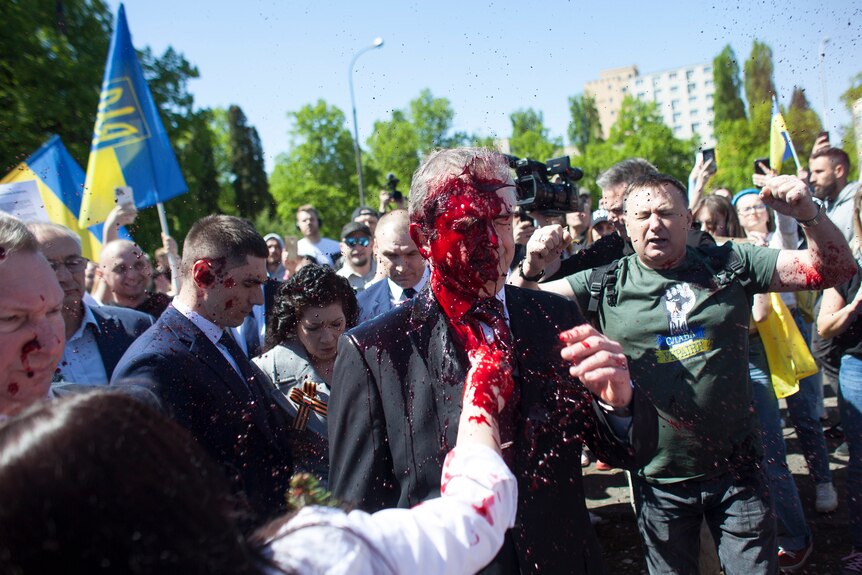 A un hombre con traje, que caminaba entre una multitud, le arrojaron pintura roja en la cara.