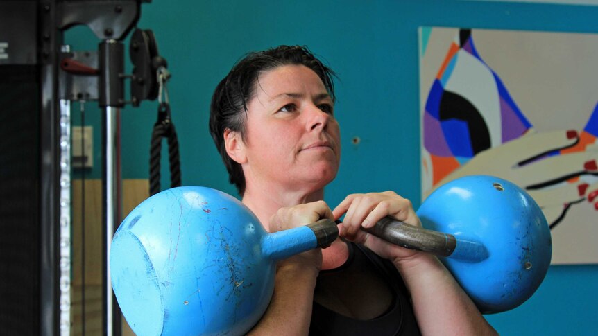 A woman holding two large, heavy kettlebells up to her chin