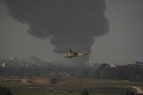 helicopter flies in front of plumes of smoke coming from Gaza strip