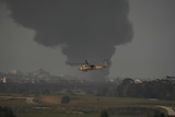 helicopter flies in front of plumes of smoke coming from Gaza strip