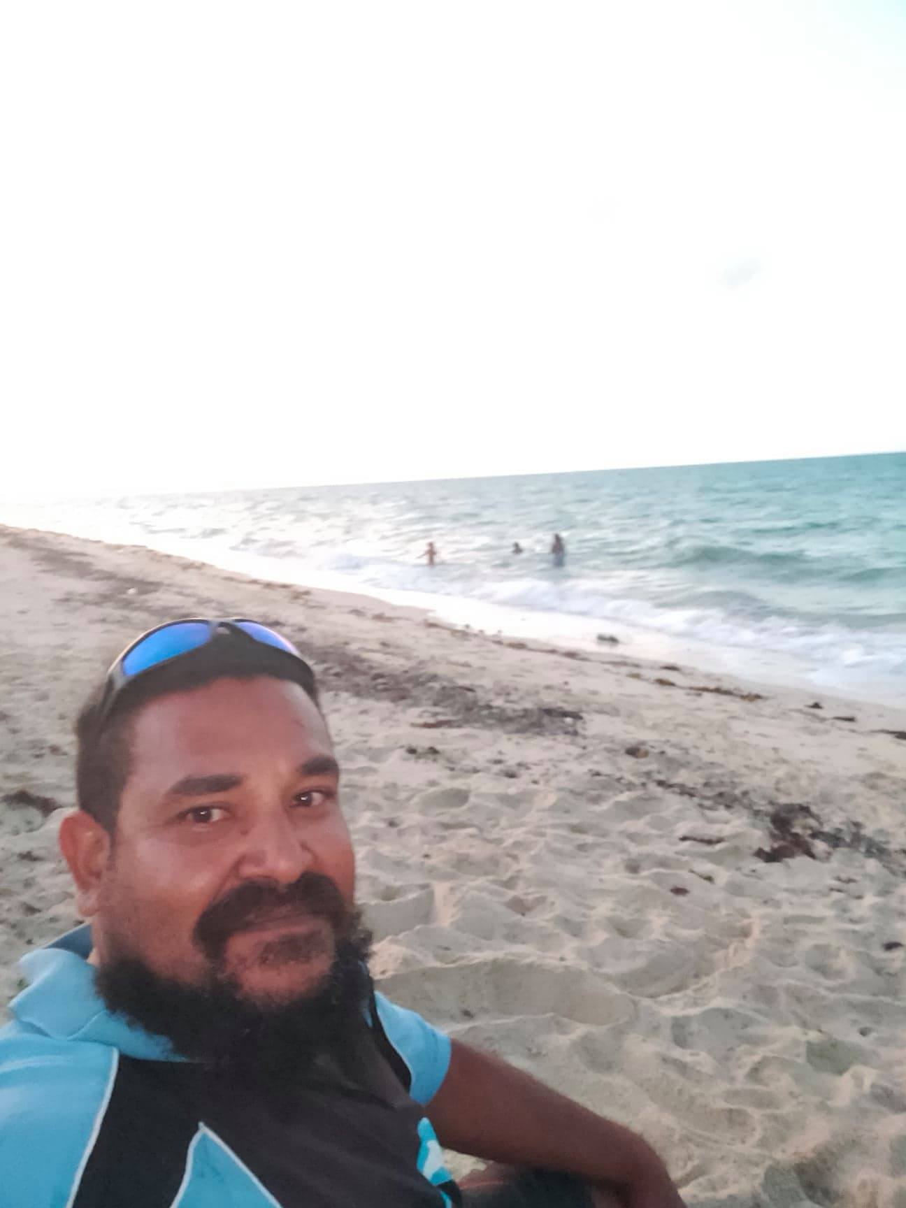 Selfie of Torres Strait Islander man sitting on beach with sea and sand in the background.