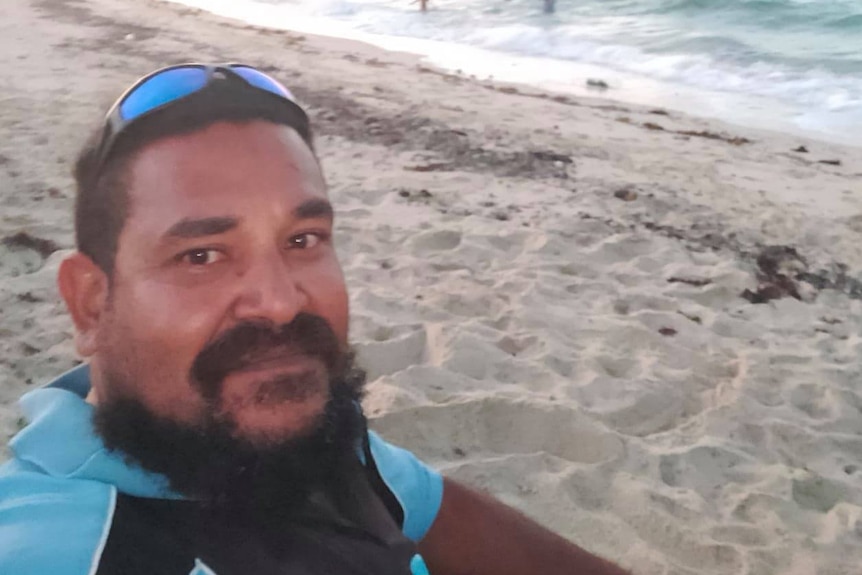 Selfie of Torres Strait Islander man sitting on beach with sea and sand in the background.