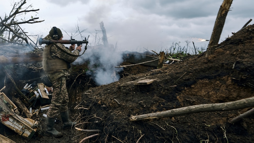 A soldier stands braced with an RPG, a fired rocket flying through the air, a scene of devastation behind him.