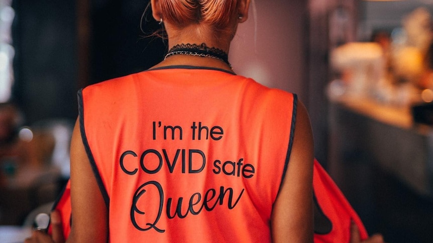 A female COVID marshall with "I'm the COVID safe queen" on the back of her high-viz vest.