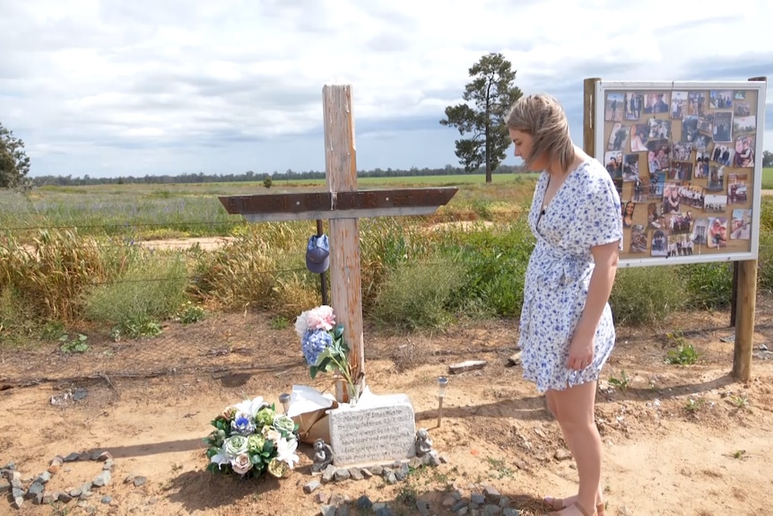 woman in dress standing and looking down at a cross and memorial near a rail line
