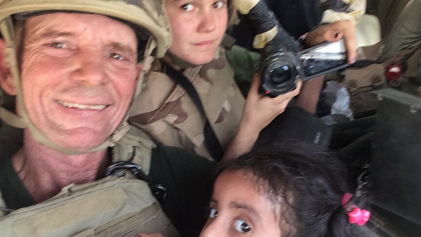 Dave and Sahale Eubank in army fatigues and helmets, with a little Iraqi girl drinking from a water bottle