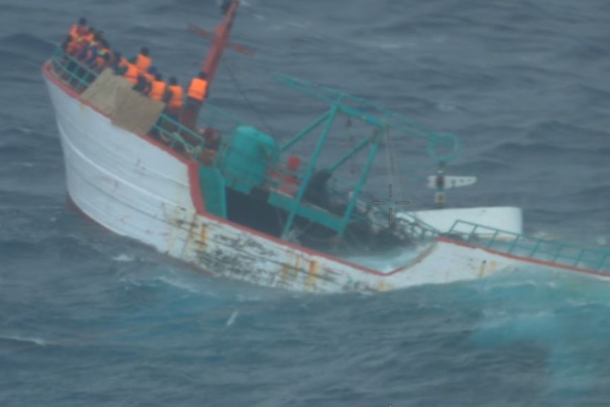 a sinking Indonesia fishing boat is shown at sea with men in lifejackets on board
