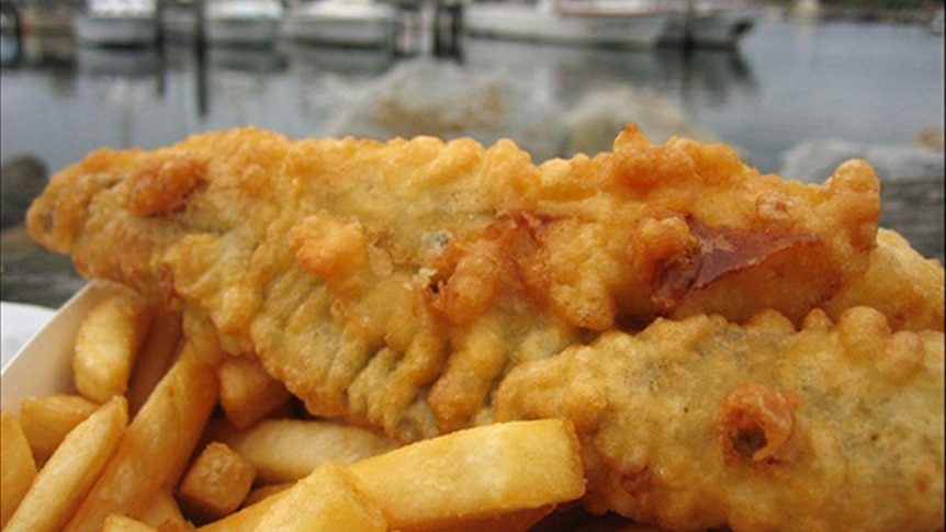 A piece of bettered fish on a plate alongside hot chips