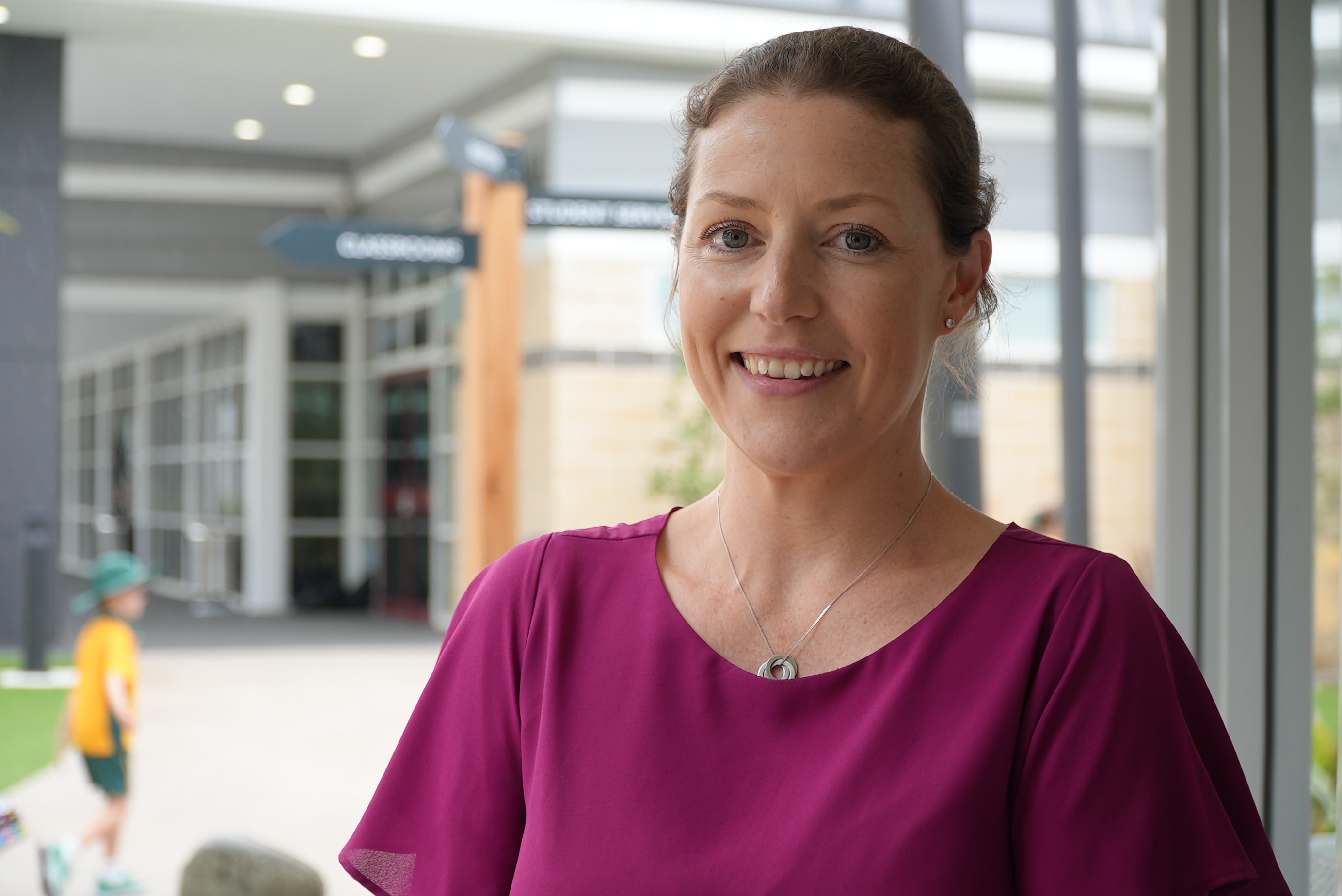 Emily Johnson wearing a deep purple top and smiling while standing in the school grounds.