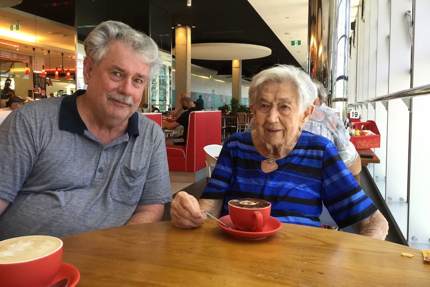 Greg Newlyn sitting at a cafe table with his mother Norma, who has a cup of coffee in front of her.