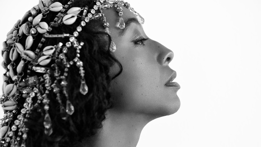 A black and white side profile image of Corinne wearing a beaded hair net. 